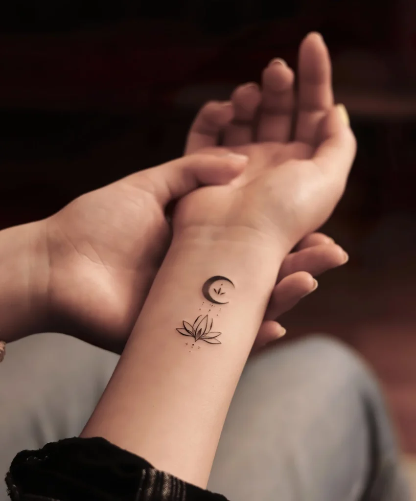 Tatouage de fleur de lotus sur le poignet avec une lune et des détails minimalistes, symbole d'élégance et de spiritualité.