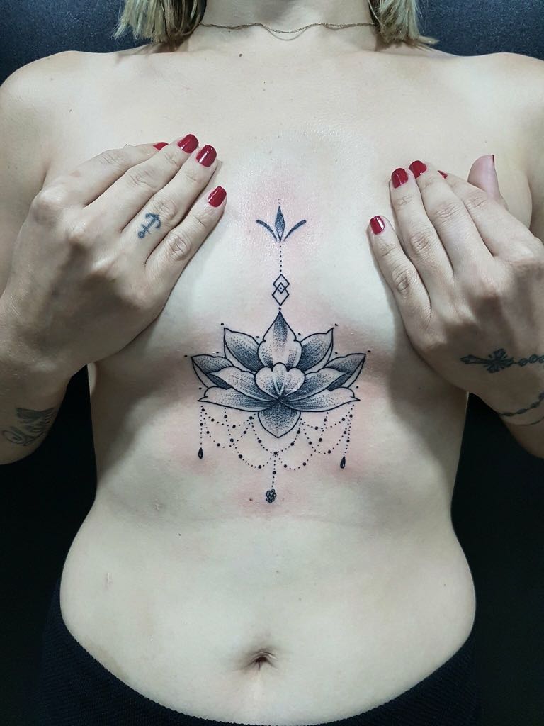 Tatouage délicat de lotus entre les seins, une idée élégante et intemporelle pour un tatouage féminin.