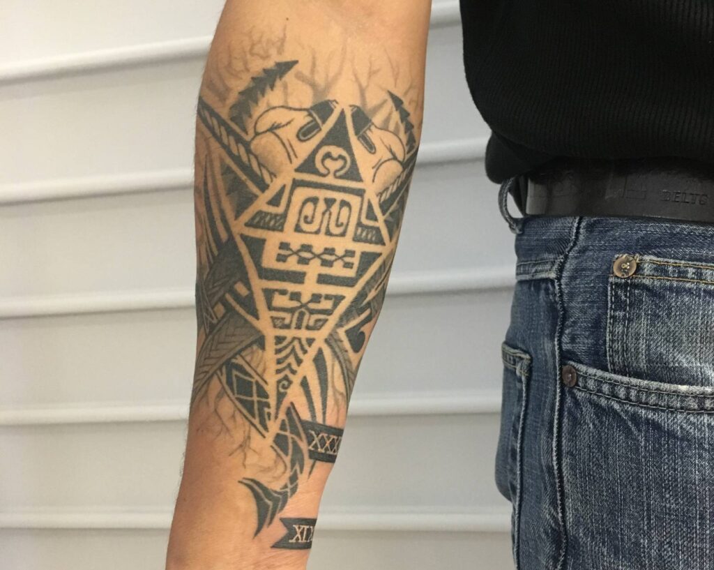 Tatouage maori détaillé sur l'épaule et le bras d'un homme, représentant des motifs traditionnels polynésiens.