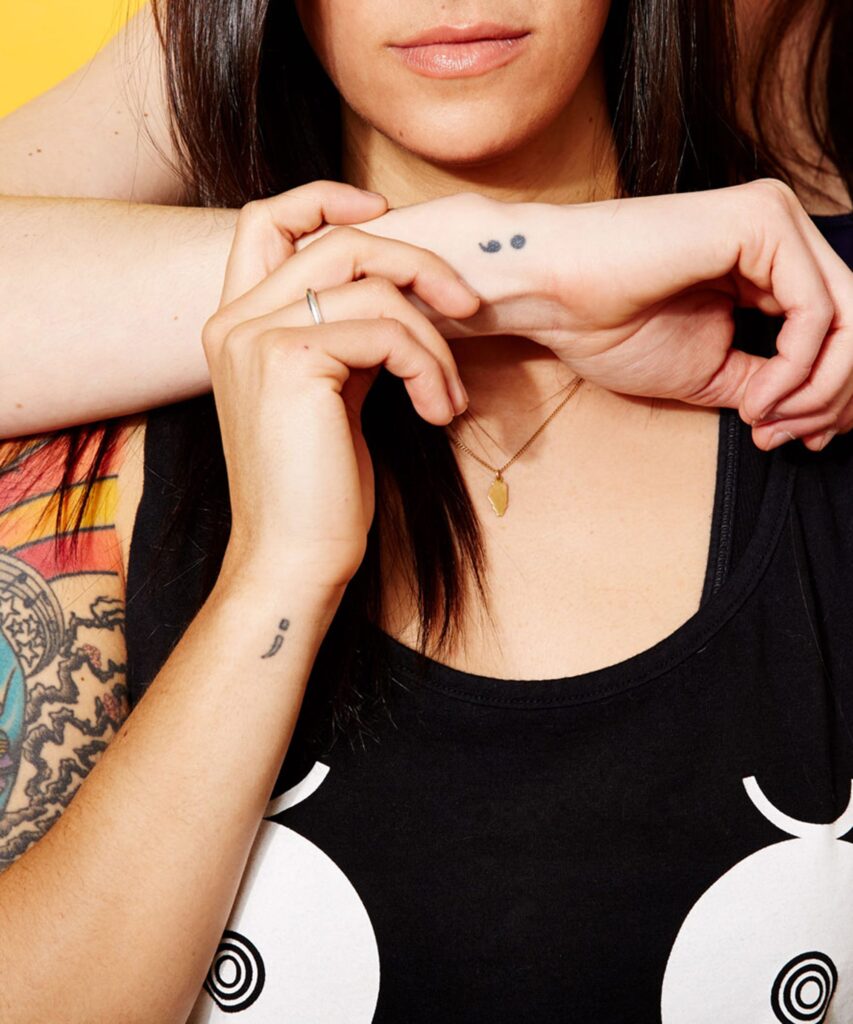 Tatouage point-virgule en noir sur un poignet, symbole de force et de résilience