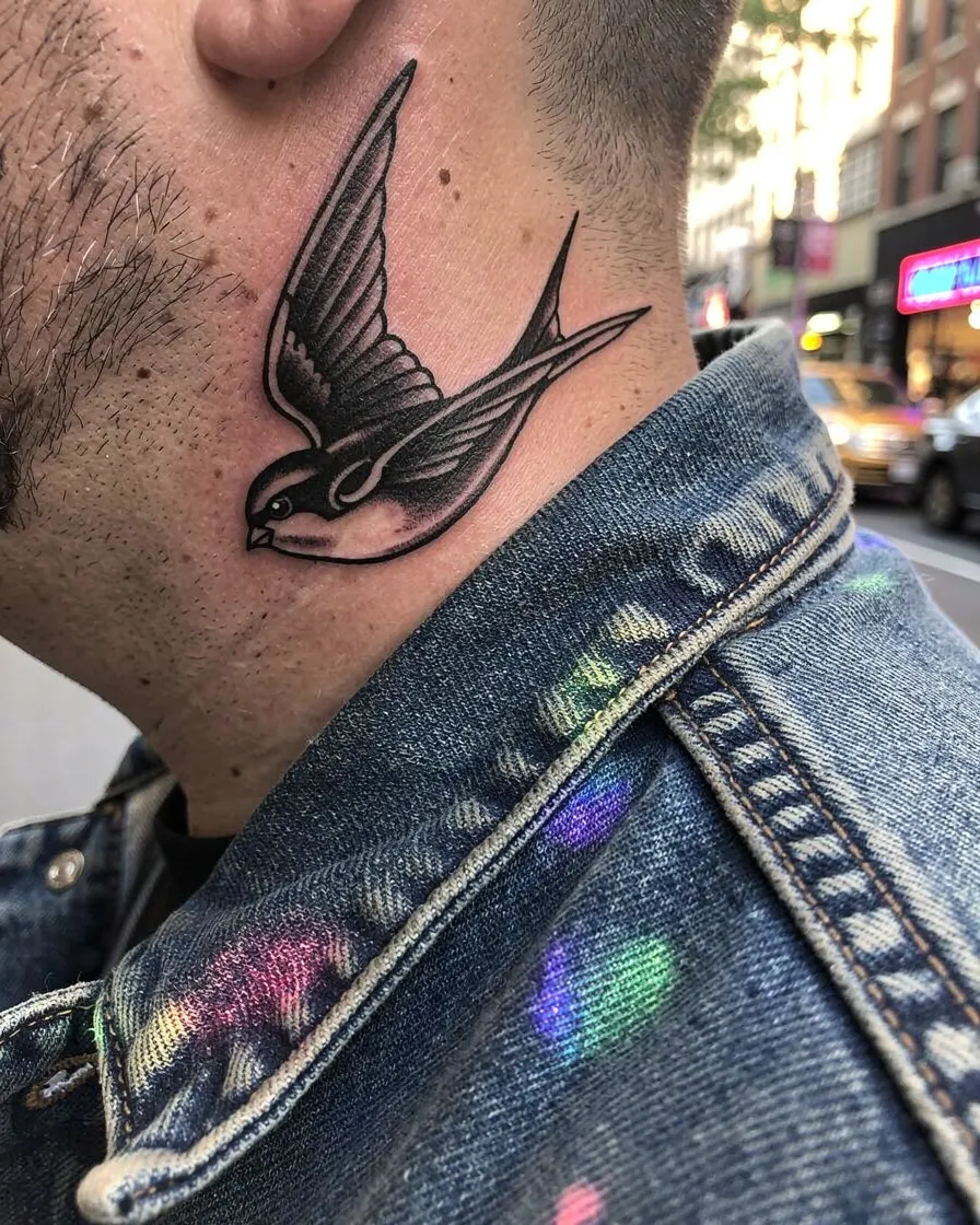 Hirondelle blackwork sur le côté du cou d’un homme en veste en jean